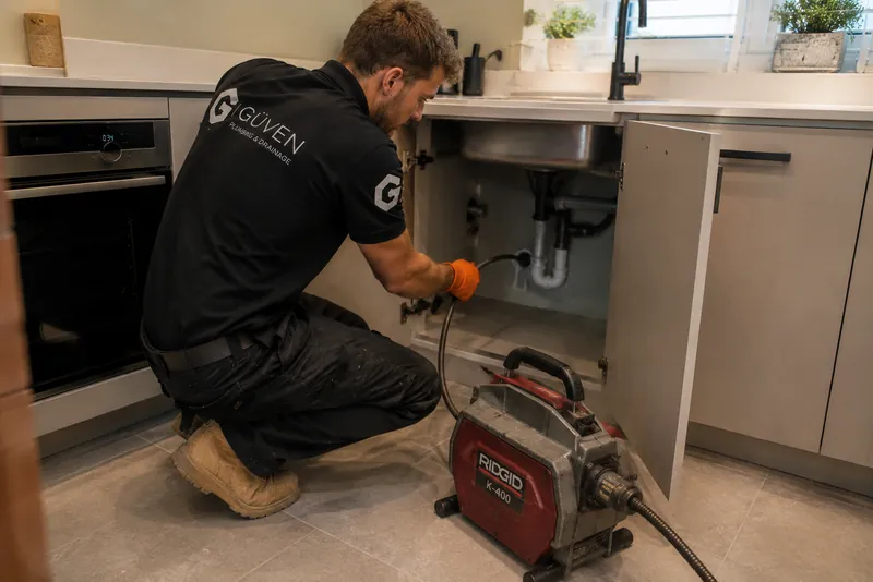Güven engineer using drain-clearing equipment beneath a kitchen sink